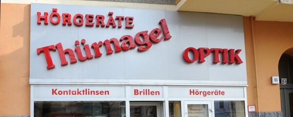 Fassade eines Optiker- und Hörgerätegeschäfts mit Schildern für Brillen und Kontaktlinsen.